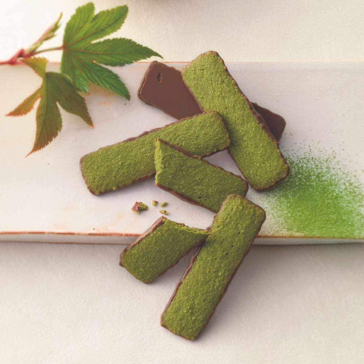 ROYCE' Chocolate - Baton Cookies "Matcha (25 Pcs)" - Image shows green cookies coated with brown chocolate on a white plate with green tea powder and some leaves for props.