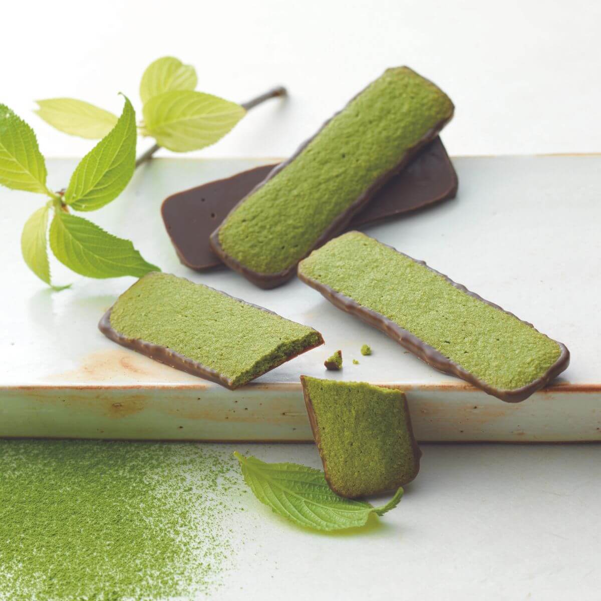 ROYCE' Chocolate - Baton Cookies "Matcha (25 Pcs)" - Image shows green cookies coated with brown chocolate on a white plate with green tea powder and some leaves for props.