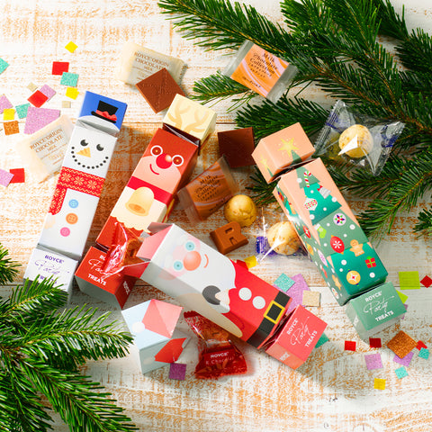 Image shows printed cylinders with accents of loose chocolates, leaves, and paper cutouts on a wooden white surface.