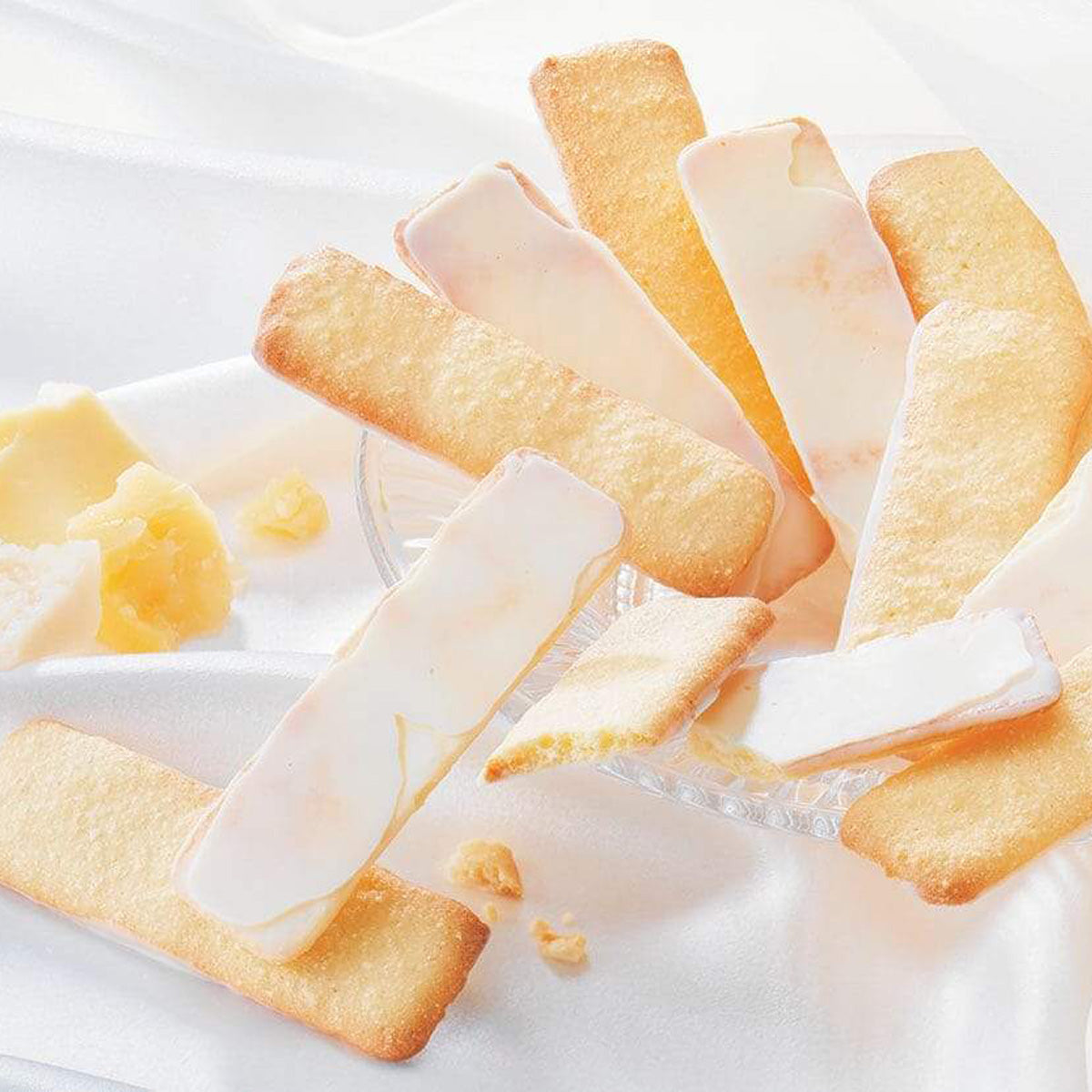 ROYCE' Chocolate - Baton Cookies "Fromage (25 Pcs)" - Image shows golden cookies coated with white chocolate on crystal bowl. Accents include blocks of cheese. Background is in white.